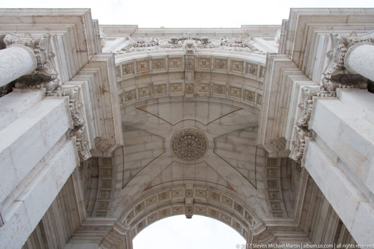 Upward view beneath the Rua Augusta Arch showing geometric coffers, molded stone panels, and a central rosette.