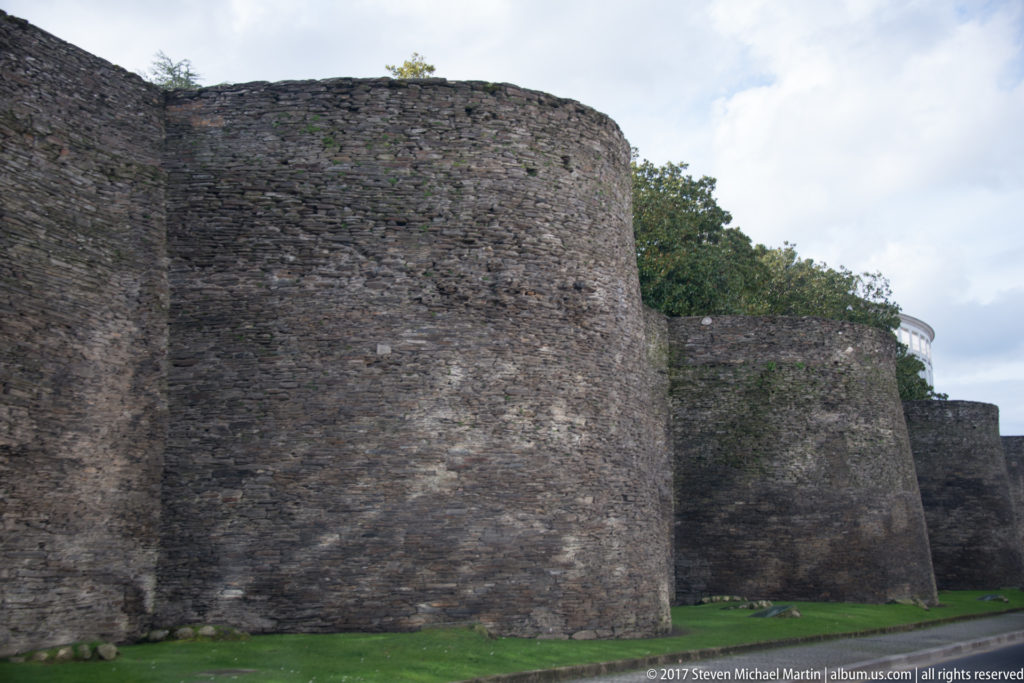 Close exterior view of massive rounded stone towers projecting from the Roman Walls of Lugo above a grass verge.