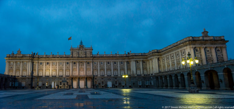 Royal Palace of Madrid illuminated across the broad Plaza de la Armería under a deep blue evening sky.