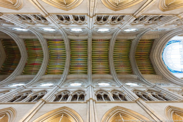 Long upward view of a cathedral barrel vault with repeated stone ribs, colorful painted panels, and clerestory openings.