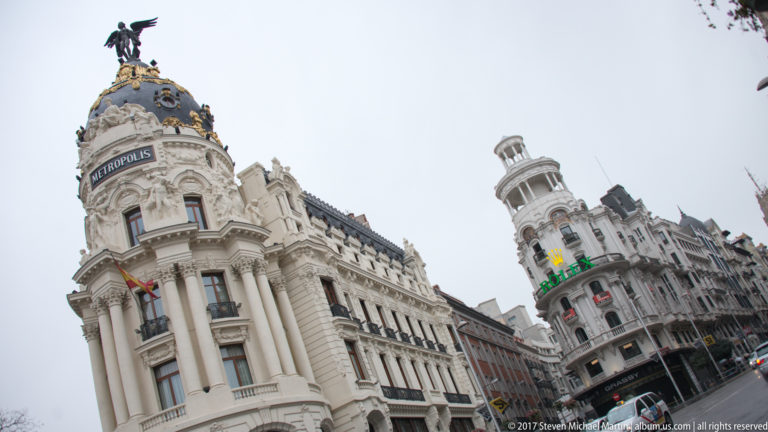 Low-angle street view of the Metrópolis Building with its domed corner tower and neighboring ornate façades.