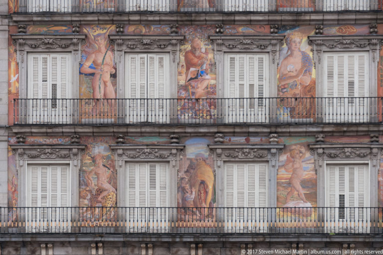 Frescoed mythological figures between shuttered windows and wrought-iron balconies on Casa de la Panadería.