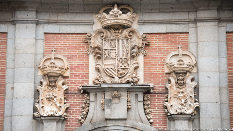 Crowned stone coat of arms with two smaller flanking heraldic sculptures mounted on a red-brick façade.