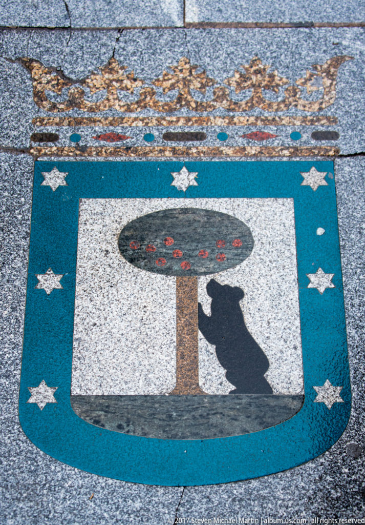 Turquoise pavement panel with a black bear reaching toward a fruiting tree, bordered by white stars.