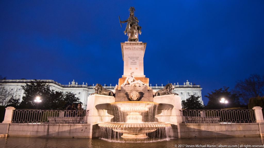 Illuminated monument to Philip IV with equestrian bronze statue above cascading fountain basins and sculpted stone figures.