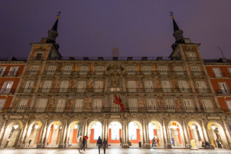 Night view of Casa de la Panadería with frescoed façade, twin towers, illuminated arcades, and red Plaza Mayor buildings.