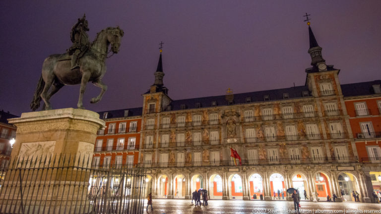 Equestrian statue of Philip III beside the illuminated Casa de la Panadería and arcaded façades of Plaza Mayor at night.