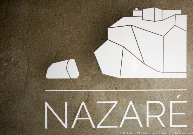 White stylized Nazaré wordmark and angular coastal landmark graphic on a dark textured background.