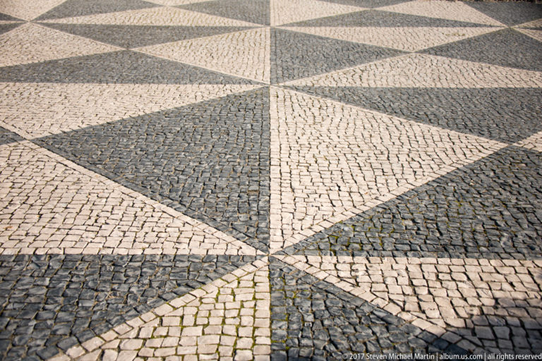 Close view of black-and-white Portuguese stone pavement arranged in radiating triangular geometric patterns.