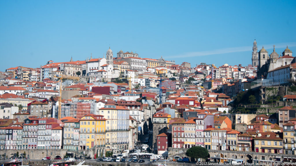 Colorful narrow buildings and red roofs densely cover Porto’s steep hillside above the Ribeira waterfront.