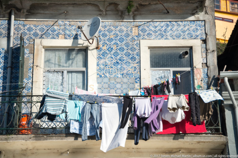 Blue-and-white azulejo tiles cover a residential façade where laundry hangs from an iron balcony between two windows.