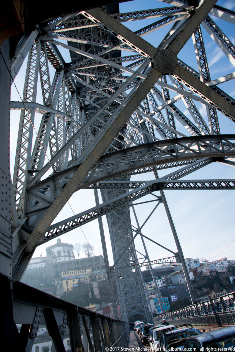 Dense riveted iron trusses and diagonal latticework fill an upward view beneath Porto’s Dom Luís I Bridge.
