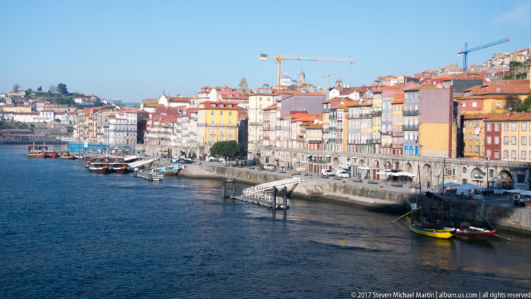 Colorful narrow façades line Porto’s curving Ribeira quay beside the Douro, with boats moored offshore.