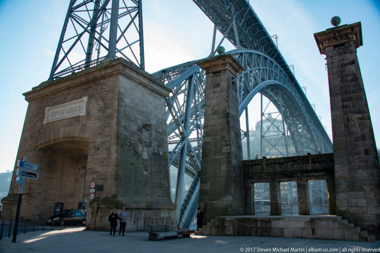 Stone portal and piers stand beneath the curving lattice ironwork of Porto’s Dom Luís I Bridge.