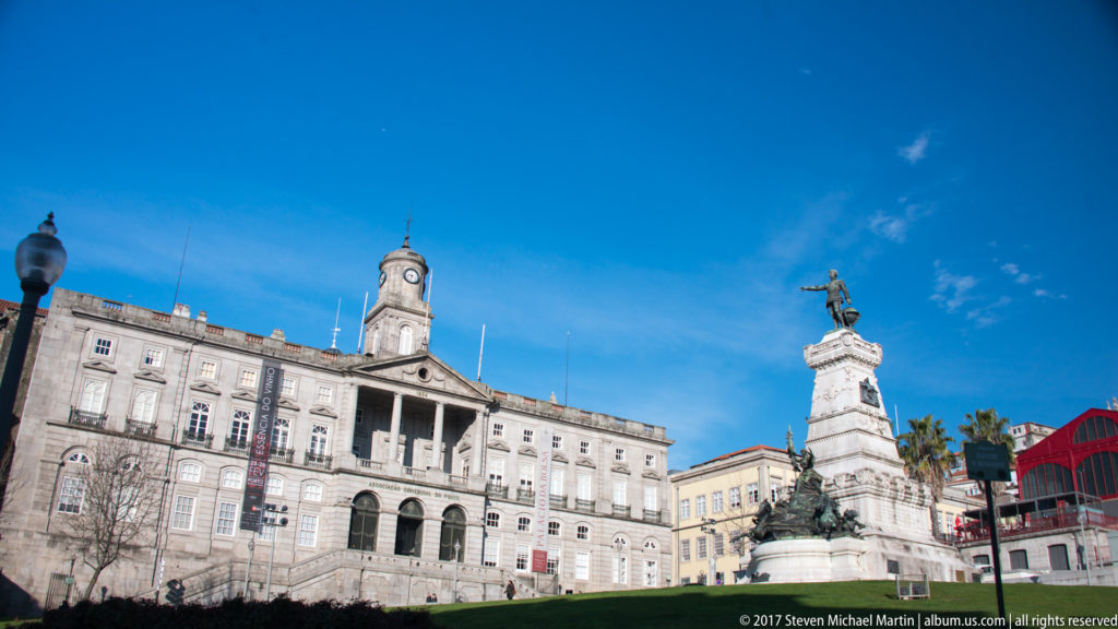 Prince Henry the Navigator monument stands before the large stone Palácio da Bolsa under a clear blue sky.