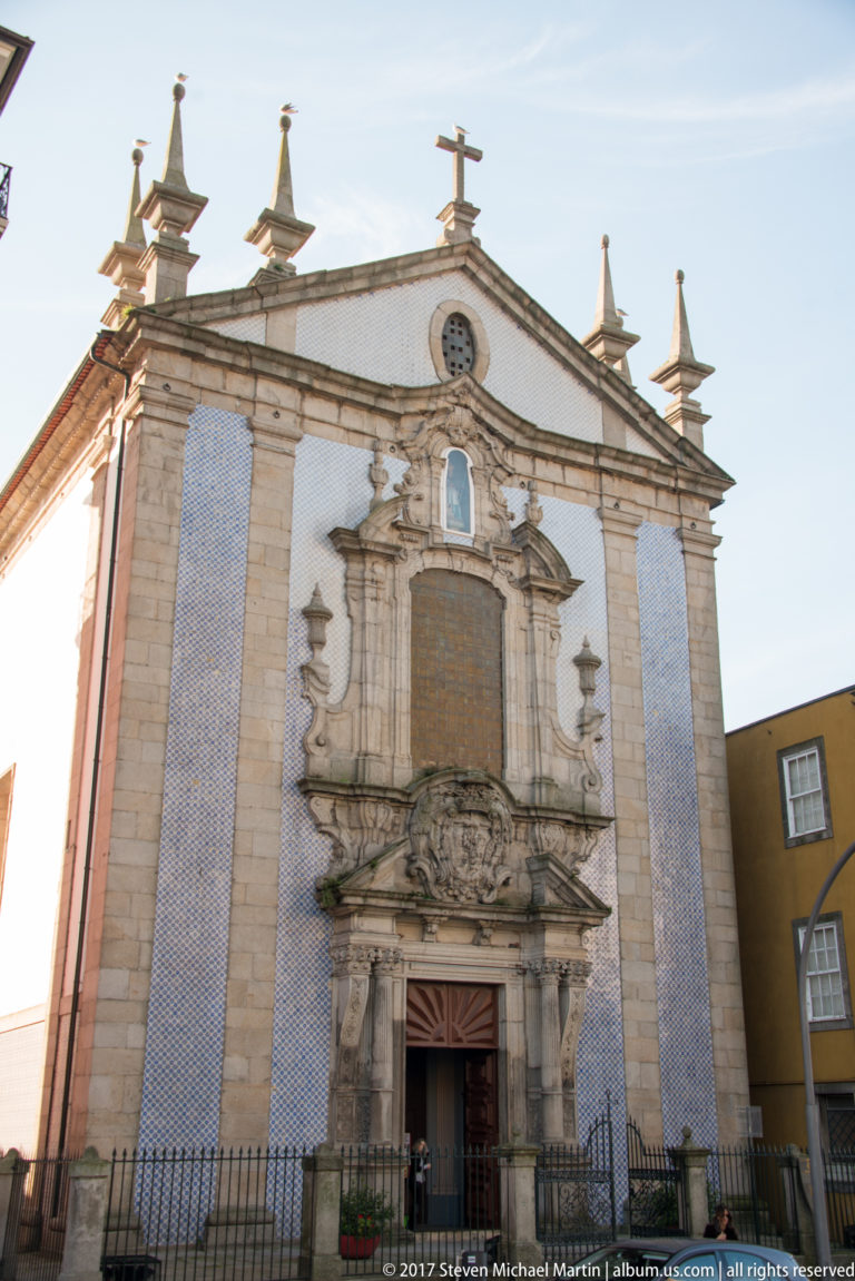 Porto church façade with blue-and-white azulejo panels, carved central portal, finials and a cross at the roofline.
