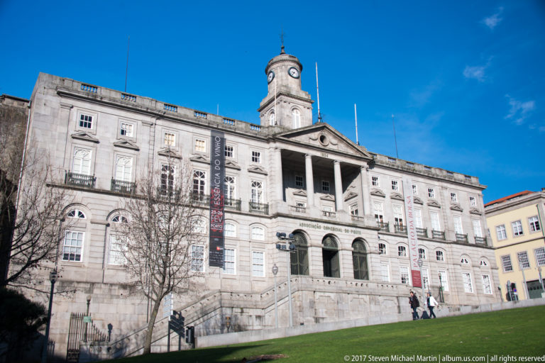 Broad stone façade of Porto’s Palácio da Bolsa with central columns, arched entrance windows and a clock above.