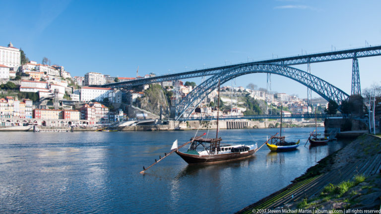 Rabelo boat near the riverbank beneath the large iron arch of Porto’s Dom Luís I Bridge.