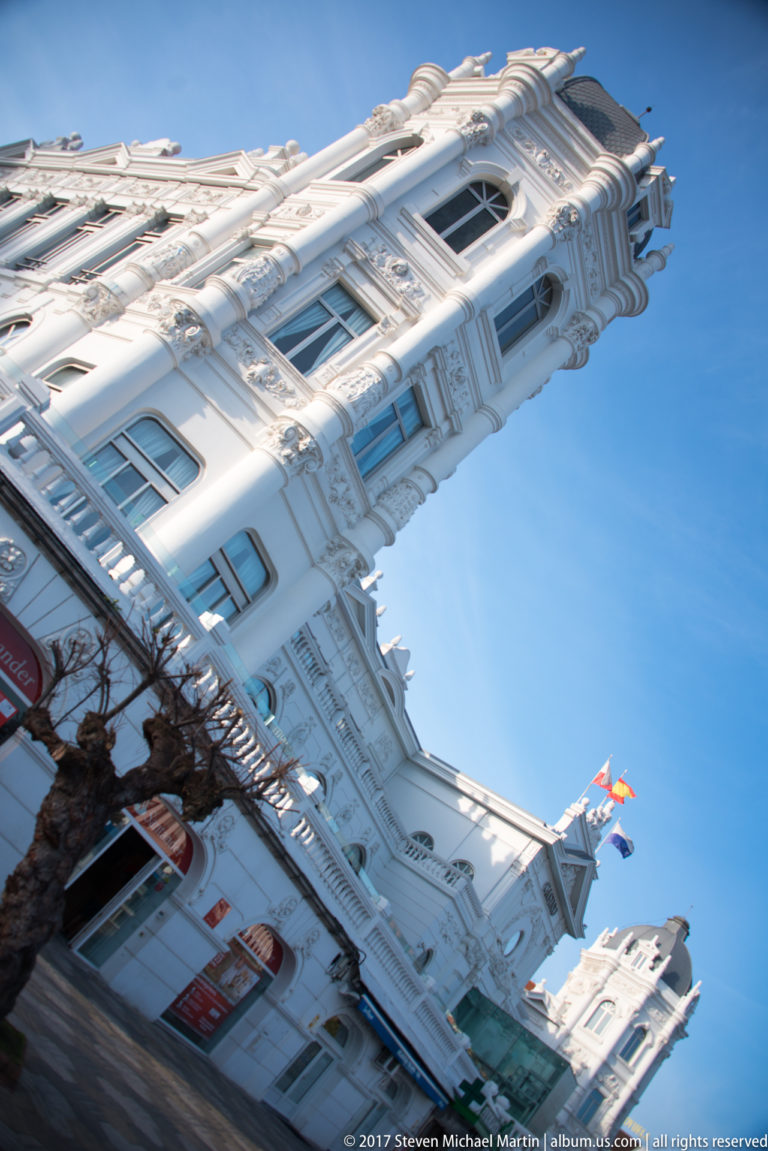 Tilted close view of Gran Casino del Sardinero corner with ornate white bays, cornices, windows, and blue sky.
