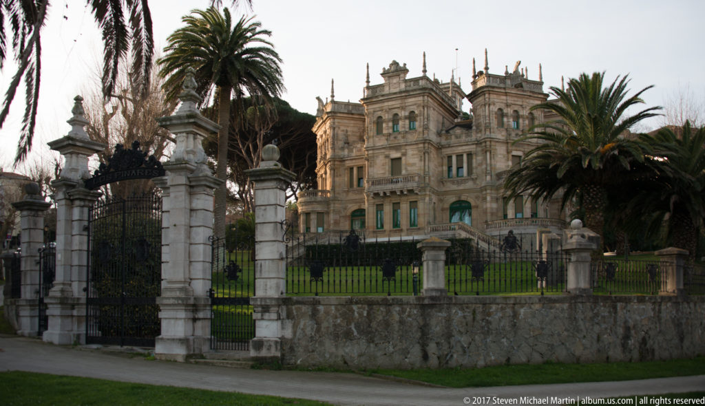 Palacio de la Magdalena seen behind wrought-iron gates, stone piers, lawns, and tall palm trees.