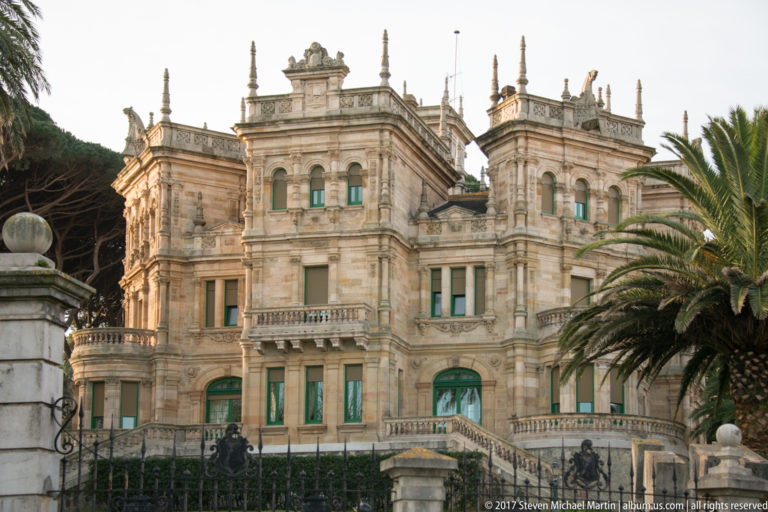 Closer view of Palacio de la Magdalena stone façades, projecting bays, terraces, tall windows, and a palm tree.