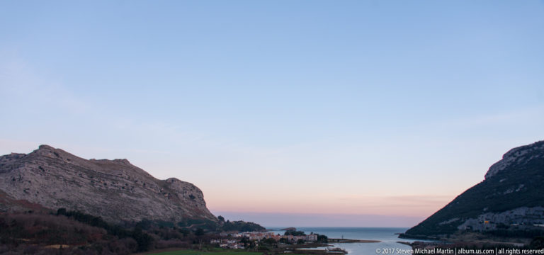 Two steep rocky headlands frame a small coastal settlement and a narrow opening to the sea.