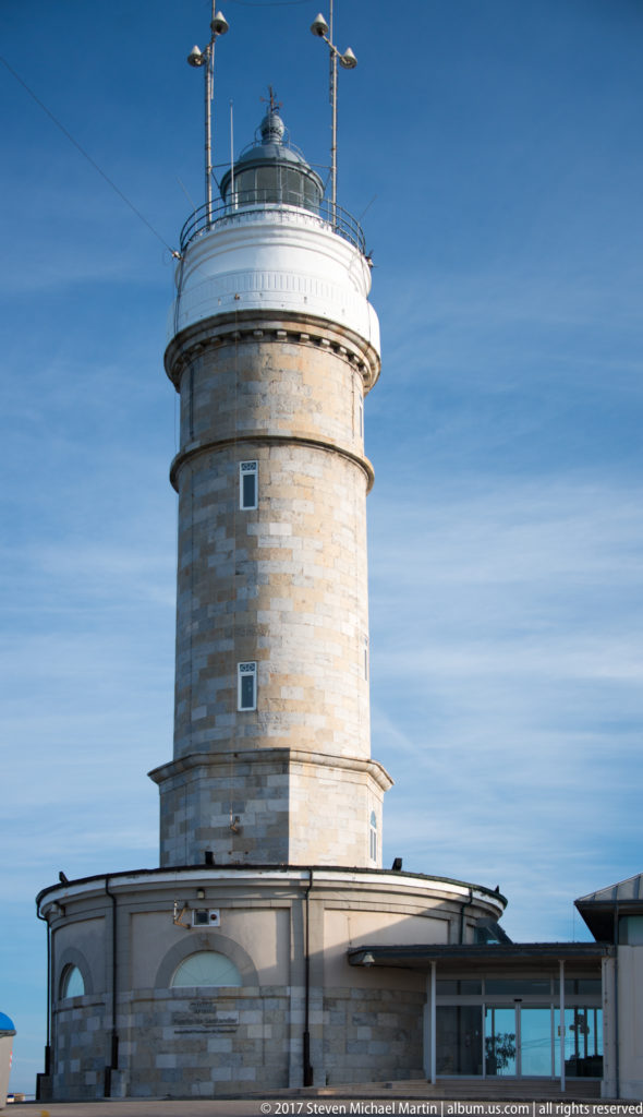 Vertical view of Cabo Mayor Lighthouse showing cylindrical stone tower, small windows, white gallery, and glazed lantern.