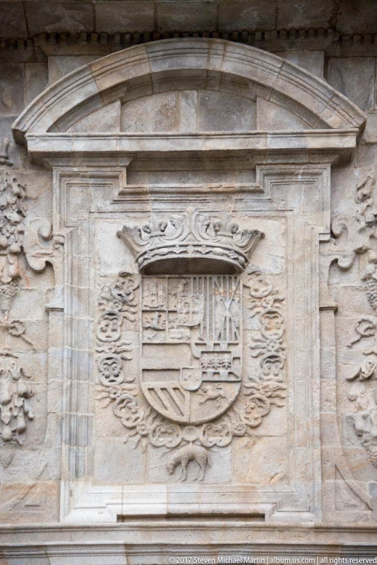 Close view of a crowned heraldic shield carved in pale stone beneath a shallow pediment.