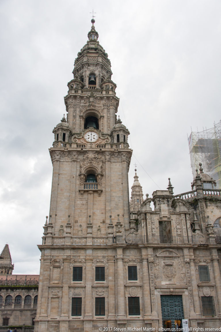 Full-height stone cathedral tower with clock and belfry rising above adjoining rooflines and smaller turrets.