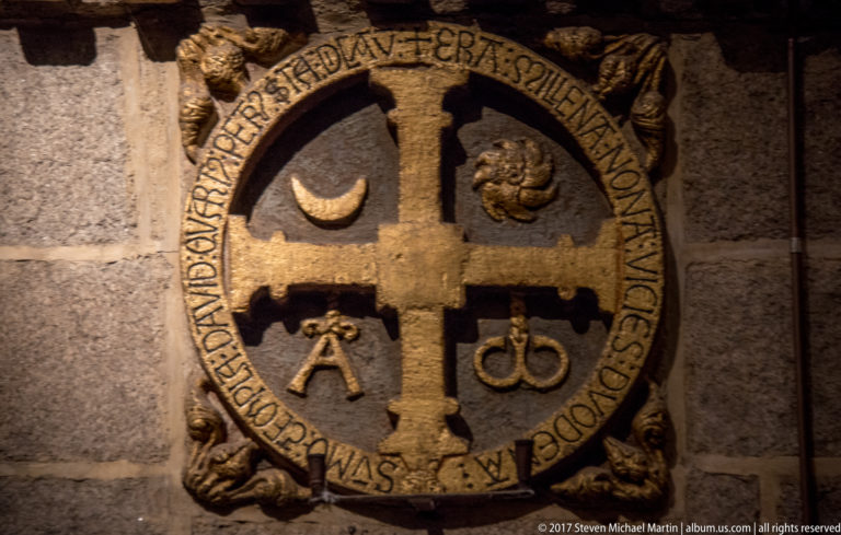 Circular emblem on a granite wall with a central cross, surrounding inscription, crescent, and other small symbols.