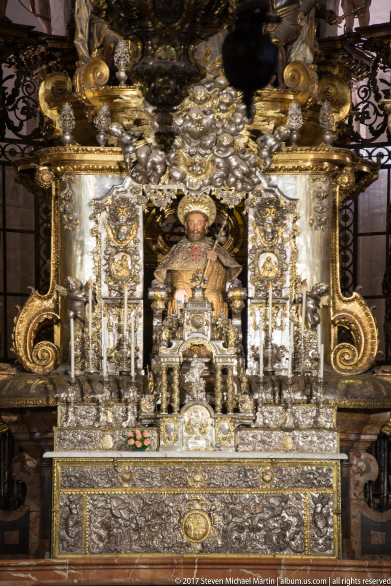 Enthroned religious figure centered above an ornate silver-and-gold altar with candlesticks and embossed metalwork.
