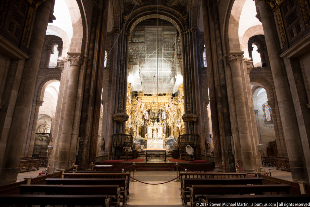 Centered nave view with pews and tall stone piers leading toward a brightly gilded sanctuary.