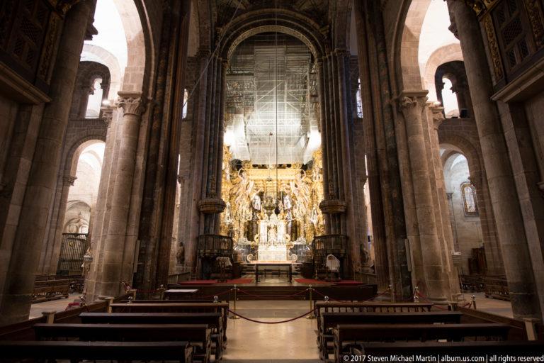 Centered nave view with pews and tall stone piers leading toward a brightly gilded sanctuary.