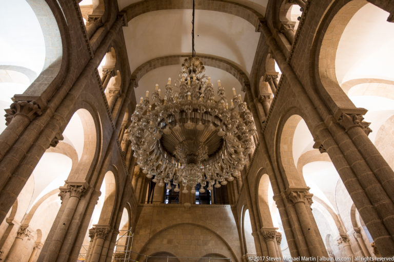 Large crystal chandelier hanging beneath intersecting stone arches, with an upper gallery visible behind.