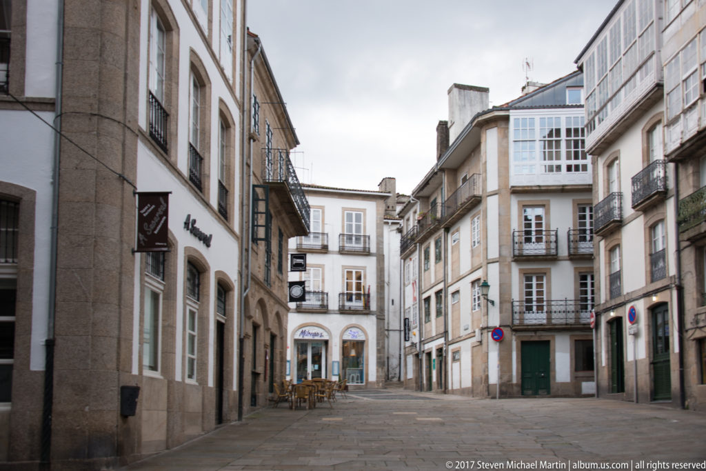Stone-paved pedestrian space lined by historic buildings with balconies, glazed galleries, shops, and café seating.