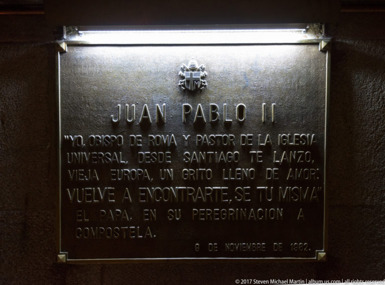Illuminated wall plaque headed “JUAN PABLO II” with Spanish text commemorating his 1982 pilgrimage to Santiago.