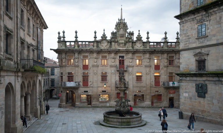 Stone plaza with a sculptural fountain, pedestrians, arcades, balconies, and ornate granite façades in central Santiago.