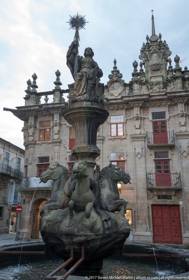 Close view of a stone fountain with four horse figures around the basin and a tall sculptural group above.