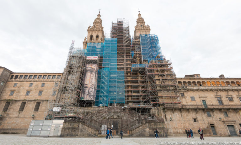 Daylight view of twin cathedral towers and a central façade enclosed in scaffolding, with pedestrians below.
