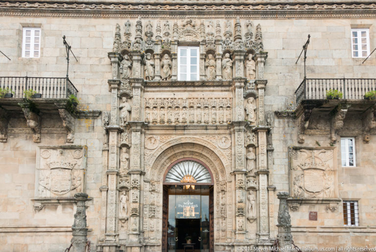 Ornate carved stone portal with tiers of statues, heraldic reliefs, pilasters, and an arched entrance in a pale façade.
