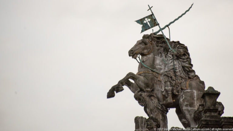 Bronze rider on a rearing horse holding a cross-bearing standard against a pale sky.