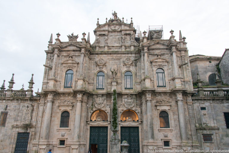 Symmetrical ornate granite façade with twin arched doorways, pilasters, carved heraldry, and an elaborate upper central section.