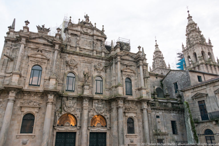 Angled view of an ornate granite façade with arched entrances and tall historic towers rising behind nearby buildings.