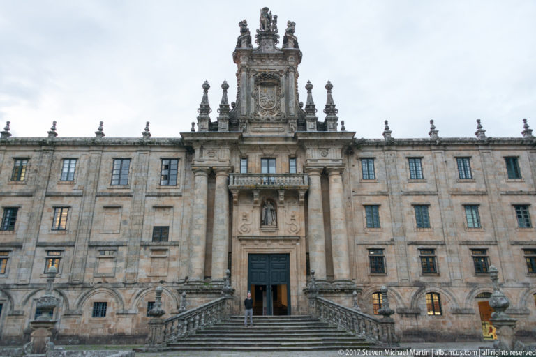 Broad granite institutional façade with central staircase, columns, balcony, heraldic carving, and symmetrical rows of windows.
