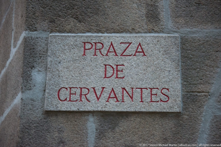 Stone wall plaque reading “PRAZA DE CERVANTES” in red capital letters.