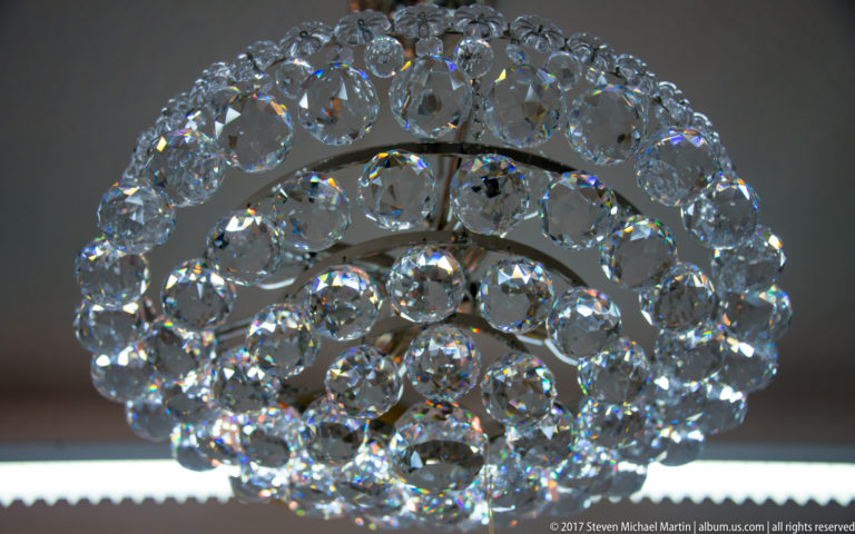 Close-up of a rounded decorative object made from concentric rings of clear faceted crystals sparkling against a dark background.