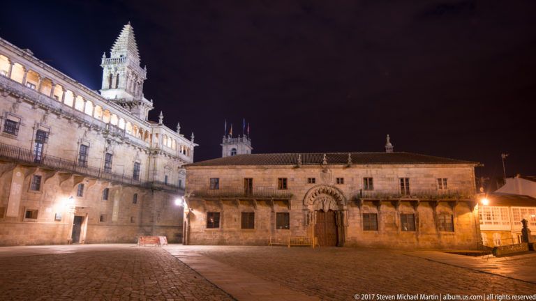 Night view of Colexio de San Xerome with carved central portal and the cathedral rising at the left edge of Obradoiro Square.