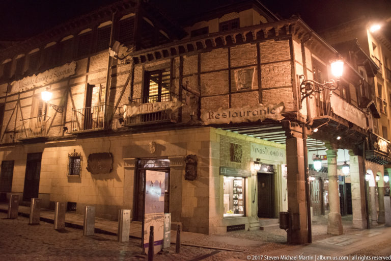 Half-timbered corner restaurant at night with wooden framing, balconies, projecting eaves, and a brightly lit street-level entrance.