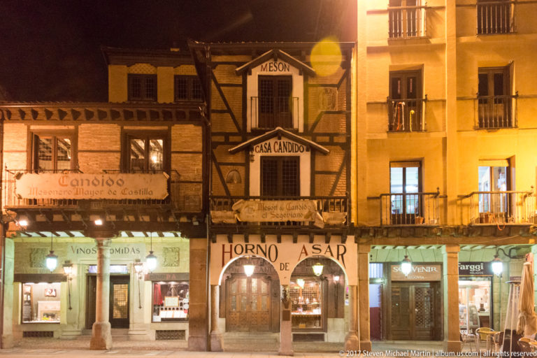 Nighttime restaurant facades including Casa Cándido, with half-timbering, balconies, illuminated entrances, and large food-related signs.