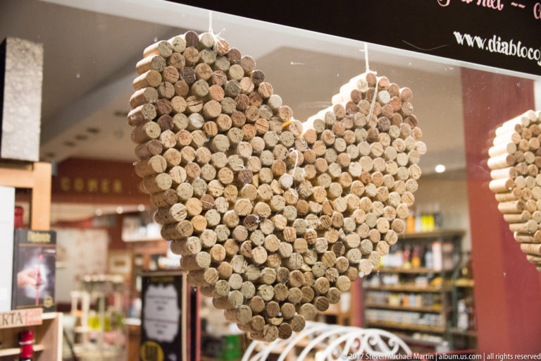 Large heart-shaped hanging decoration made from dozens of wine corks, suspended in front of a shop or restaurant interior.